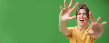 Komik, duygusal bir kadın, yüzünü ekşiterek, çatık kaşlı, ağzı açık, kameradan yüzünü gizlemek isteyen, yeşil arka planda somurtan bir şeyin saldırısına uğruyor. Vücut dili ve duyguları