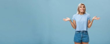 Oops, bilmiyorum. Sarı saçlı, havalı dövmeleri olan, avuçlarını yana açmış, avuçlarını silkeleyen, üzgün gülümseyen aptal Avrupalı kız. Mavi duvardan habersiz ve cahil görünüyor..