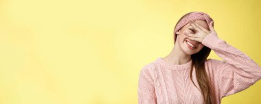 Utangaç tatlı kız pozitif hissediyor, mutlu mutlu neşeli kaplama gözleri parmaklarının arasından süzülüyor keyifli, şakacı, eğimli başı hassas ve sevimli bakışları sarı arka plana bakıyor..