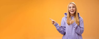 Karizmatik, yakışıklı, sarışın, solu işaret eden genç bir kız. Muhteşem yeni restoranı tartışıyorlar. Arkadaşına gülümseyerek, turuncu arka planda gülüşünü kontrol etmesini söyle..