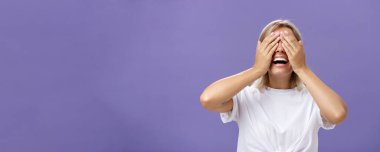 Şimdi bakabilir miyim? Heyecanlı, mutlu, bronz tenli, beyaz tişörtlü, gözlerini kapayan ve gülümseyen bir erkek arkadaşın portresi mor arka planda sürpriz hediyeler getiriyor..