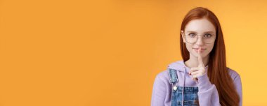Şşş gizli kasa. Genç, şehvetli, gizemli, kızıl saçlı, bilgi saklayan çekici kadın sessiz olun diyor. Lütfen sürpriz bekleme parmaklarını hazırla. Ağız tabusu, ayakta duran turuncu arka plan..