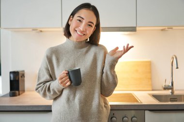 Asyalı şık bir kadının portresi mutfakta elinde fincanla duruyor, kahve içiyor, smth 'yi açıklıyor, pankart ya da reklam gösteriyor..