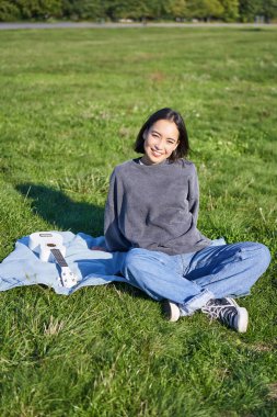 Yüzünde ukulele gitarla battaniyeye oturmuş güneşli bir günde parkta dinlenen Asyalı kızın dikey görüntüsü..