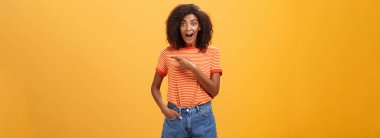 Hey harika kopyalama alanı. Etkilenmiş ve şaşırmış Afro saçlı Amerikalı genç bir kadının portresi turuncu duvarın üzerinde enerjik ve meraklı bir görünüm sergiliyor.