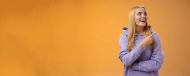 Neşeli, neşeli, kapüşonlu, neşeli Avrupalı kadın gülümseyen mutlu bir gülümseme ile dükkan alışverişinde ilginç bir performans sergiliyor, turuncu arka plan.