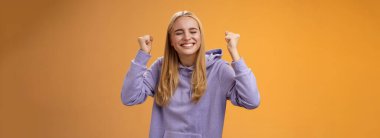 Pozitif saçlı genç kadın kazananın zaferini kutlarken ellerini kaldır zafer elde etmek için ellerini yumruk at. Gözlerini kapat ve gülümseyerek büyük teklifi kabul et, başarıya ulaş..