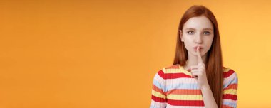 Kız çok sır saklıyor. Ciddi görünümlü kızıl saçlı kız arkadaş mavi gözler sessiz olun sessiz olun sessiz olun sessiz hareket işaret parmağı bastırılmış dudaklar, sürpriz hazırlan turuncu arka plan.