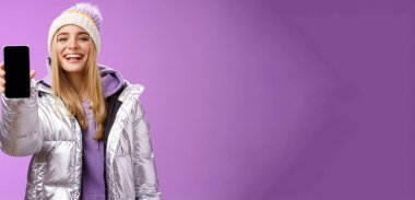 Şımarık, neşeli, sarışın bir kadın elinde cep telefonu görüntüsü, gururla tatmin edici gülümseme kamerası, ayakta duran mor arkaplan gösteren akıllı telefonları kullanarak uygulamayı düzenlemeyi öneriyor..