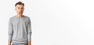 Beyaz saçlı, kafası karışmış, korkmuş, ağzı açık, beyaz arka planda duran ve kameraya bakan orta yaşlı yakışıklı bir adamın portresi..