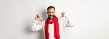 Kış tatili ve alışveriş konsepti. Kendine güvenen sakallı adam, mutlu bir şekilde gülümsüyor, kırmızı atkı ve süveterle Noel 'i kutluyor, beyaz arka planda..