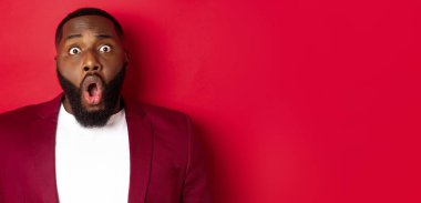 Şok olmuş, soluk soluğa kalmış, çenesi düşmüş, kameraya bakan, kırmızı arka planda duran siyahi adamın yakın çekimi..