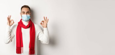 Covid-19, tecrit ve karantina konsepti. Yüz maskesi takmış tatmin olmuş yakışıklı bir adam işaret veriyor, onaylıyor ya da kabul ediyor..