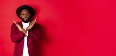 Ciddi siyahi adam görüntüsü buna şiddetle karşı çıkıyor, çapraz işaret gösteriyor, bir şeyi yasaklıyor, kırmızı arka planda duruyor..