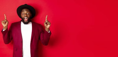 Kış tatili ve alışveriş konsepti. Parti kıyafetli neşeli Afro-Amerikalı adam logoyu gösteriyor ve gülümsüyor..