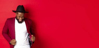 Noel ve insanlar kavramı. Mutlu siyah adam yeni yılı kutluyor ve dans ediyor, parti kıyafeti giyiyor, kırmızı arka plan.