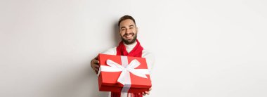 Kış tatili kavramı. Yakışıklı erkek arkadaş hediye veriyor, mutlu noeller diliyor ve beyaz arka planda duruyor..