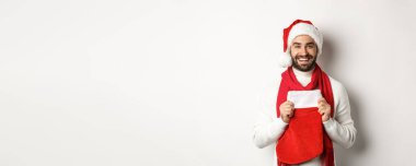 Kış tatili ve alışveriş konsepti. Yakışıklı sakallı adam Noel çorabında hediyeler getiriyor, gülümsüyor ve mutlu yıllar diliyor, beyaz bir geçmişi var..