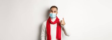 Covid-19, tecrit ve karantina konsepti. Yüz maskesi takmış tatmin olmuş gülümseyen bir adam beyaz arka planda duran, başparmağını kaldıran, onaylayan ya da ürün gibi görünen.