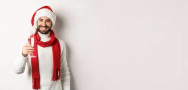 Noel partisi ve tatil konsepti. Sakallı yakışıklı genç adam, yeni yıl arifesinde kadeh kaldırıyor, elinde bir bardak şampanya ve gülümsüyor, beyaz arka plan.