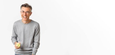 Mutlu ve sağlıklı orta yaşlı bir adamın resmi, yeşil bir elma tutuyor, gülüyor ve kaygısızca gülümsüyor, beyaz arka planda duruyor..