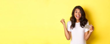 Mobil oyunda kazanan güzel Afro-Amerikalı kız imajı, uygulamada hedefe ulaşmak, sarı arka planda mutlu durmak.