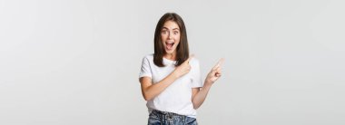 Heyecanlı güzel kız gülümsüyor, parmaklarını sol üst köşeye gösteriyor ve logodan memnun görünüyor..