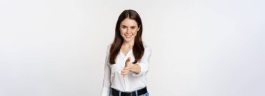Smiling, friendly corporate woman extending arm for handshake, shaking hand, greeting business partner, standing over white background.