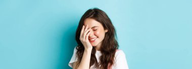 Gülümseyen, gülümseyen, gülümseyen, gülümseyen, mavi arka planda duran güzel, genç bir kadın..