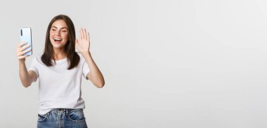 Arkadaş canlısı çekici kız merhaba diyor, video görüşmesi sırasında akıllı telefona el sallıyor, sohbet ediyor..