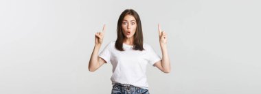 Şaşırmış ve etkilenmiş esmer kız şaşkın şaşkın bakıyor ve parmakla işaret ediyor..