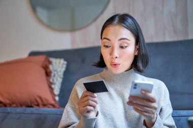 Akıllı telefon uygulamasında kredi kartıyla ödeme yapan gülümseyen Asyalı kadının portresi, cep telefonundan doğrudan banka hesabı ya da internet üzerinden alışveriş ayarlamak.