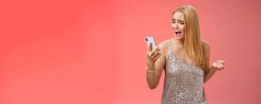 Troubled concerned arrogant young blond woman complaining yelling smartphone cannot call friend no signal holding smartphone look mobile display pissed moody arguging, red background.