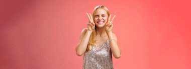 Heyecanlı, mutlu, neşeli, Avrupalı, neşeli sarışın kadın eğleniyor, kokteyller içiyor, gece kulübünde dans ediyor, gülümseyen, kapalı gözler barış tavşanı hareketini kırmızı arka planda gösteriyor. Boşluğu kopyala