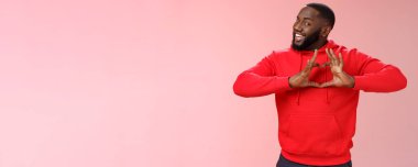 Biri seni seviyor. Kırmızı kapüşonlu giyinen, hevesli, yaratıcı, siyah bir erkek arkadaş. Gülümseyen, sevgisini itiraf eden bir kalp işareti. Tutkulu görün, romantik pembe arka plan..