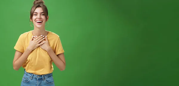 stock image Delighted charming woman with gapped teeth in cozy outfit holding palms on chest in grateful or thankful pose smiling broadly receiving warm congratulations standing satisfied, happy over green wall