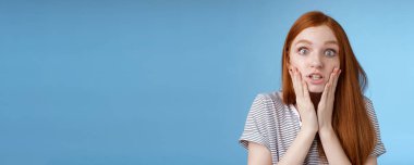 Shit bummer. Shocked worried young intense serious-looking confused young redhead girl look stressed nervously touching face wide eyes staring camera anxiously, standing blue background.