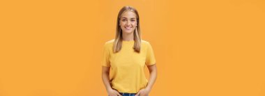 Bronzlaşmış tenli, açık tenli, turuncu arka planda iyimser ve neşeli poz veren sevimli tombul kadın kameranın karizmatik ve arkadaş canlısı görünüşüne gülümseyen ceplerinde el ele tutuşuyor. Yaşam biçimi.