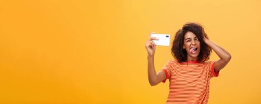 Şık, kendine güvenen Afro saçlı, modaya uygun tişörtlü, fotograf çeken, dilini dışarı çıkaran, saçlarıyla oynayan ve akıllı telefona göz kırpan Afro-Amerikan kadının belden yumağı fotoğrafı.