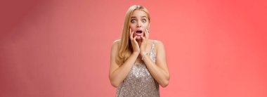 Şok olmuş genç Avrupalı, şaşkın, genç, sarışın kadın gümüş önlüklü, çenesi açık, ağzı açık, ağzı açık, ağzı açık, şaşkın, kafası karışmış, kırmızı arka planda..