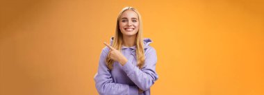 Karizmatik modern çağdaş sevimli kapüşonlu sarışın kadın mutlu bir şekilde yeni tanıtımını tartışıyor sağ köşedeki ilginç mağazayı kontrol edin, turuncu arka plan..