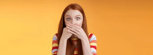 Oops sorry. Girl feeling awkward saying inappropriate word standing unconfident cover mouth palms wide eyes staring camera shocked express surprise nervously standing orange background.