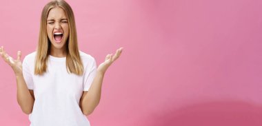 Woman feeling fed up having mental breakdown during deadline yelling with closed eyes, raising hands aside in pissed gesture feeling distressed and pressured losing temper over pink wall. Emotions