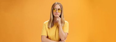 Sorunlu ve endişeli genç bir kadın sorunlu bir sorunla karşı karşıya. Çene üzerinde el ele tutuşup dudaklarını büzüyor. Sağ üst köşeye dikkatlice bakıyor.