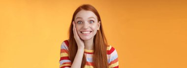 Neşeli, mutlu, heyecanlı, kızıl saçlı, kızaran, mutlu, mutlu, dokunaklı, mutlu, sevinçli, sevinçli, heyecanlı, turuncu arka planda poz veren güzel bir kız..