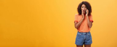 Rahatsız edici bir çağrı alan empatiyi hisseden kadın ve zavallı arkadaşının başı derde girdiği için üzgün. Kulağının dibinde cep telefonu tutmakta, yanaklarına dokunmakta, üzgün durmakta, turuncu arka plan için endişelenmekte..