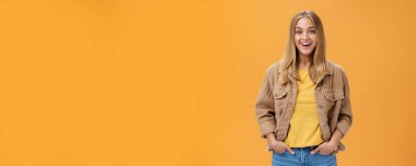 Kadife ceketli, sarı tişörtlü karizmatik bir kadın serin sonbahar yürüyüşüne hazır. Arkadaşları sevinçle gülümsüyor, kameraya bakıyor turuncu duvarın üstünde el ele tutuşuyor.