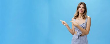 Stüdyo çekimlerinde hoşnutsuz bir kadın işaret parmağıyla işaret ederek tiksindirici ve tatminsiz bir ifadeyi işaret ederek tiksindirici ve korkunç bir şeyi mavi arka planda görmekten iğreniyor.