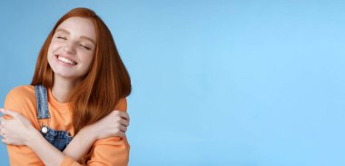 Yaşam tarzı. Yakın plan mutlu, mutlu, kızıl saçlı, gözleri kapalı romantik bir randevu hayal eden, beyaz dişleri sırıtan, kollarını kavuşturan, kucaklayan, güzel anıları hatırlatan, sarılan, hayal kuran bir kız..