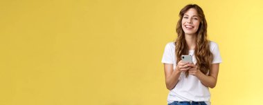 Canlı, coşkulu, güler yüzlü, mutlu kadın akıllı telefon mesajları, mesajlaşma arkadaşı sosyal medyayı kontrol ediyor internette geziniyor cep telefonunu tutuyor mutlu, sarı arka planda gülüyor..